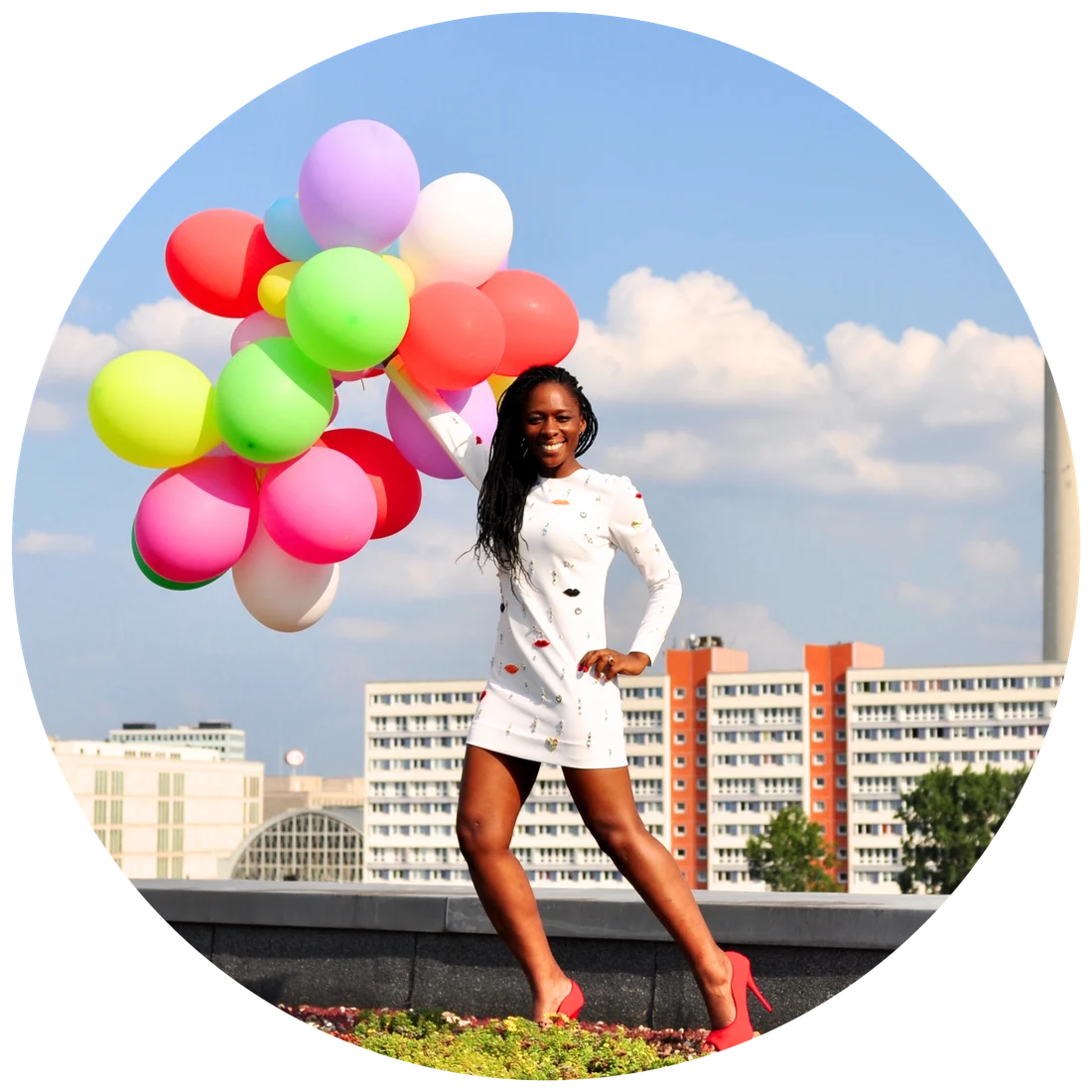 A smiling person holding colourful balloons in front of the Berlin skyline